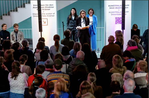 Drei Frauen stehen auf dem Podium vor Publikum.